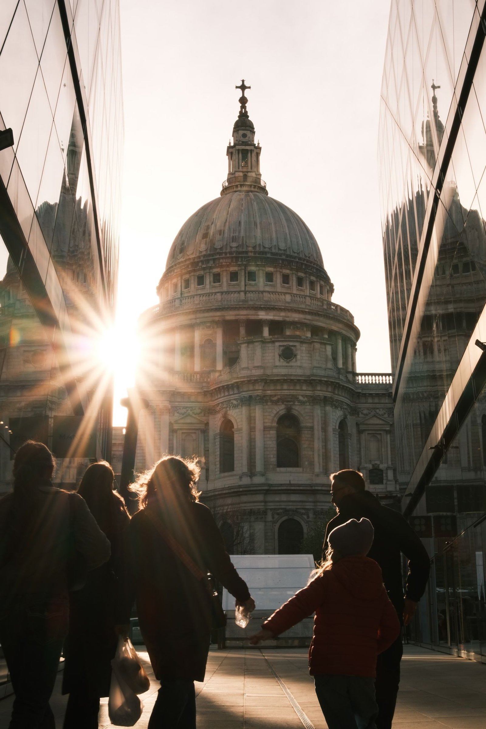 A family walks past St. Paul's Cathedral in London during sunset, creating a striking silhouette.